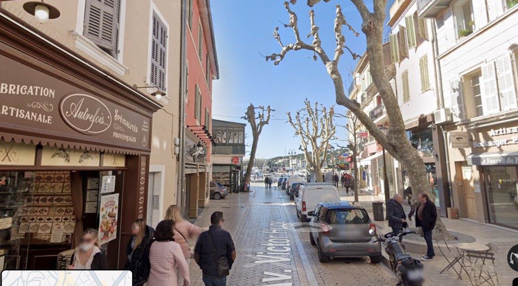 A narrow Cassis street: shops, café tables, people walking, one parked car