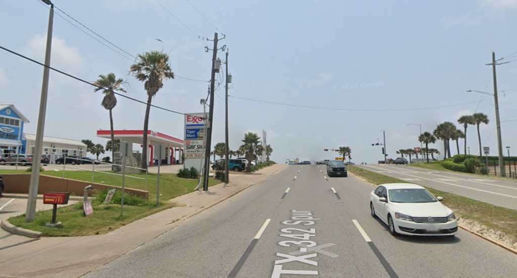 A wide Galveston highway with a gas station, palmettos, and almost no one walking
