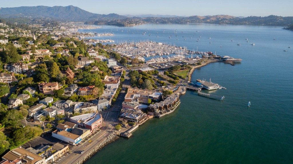 Aerial of downtown Sausalito: ferry pier, lawn, surface parking, and a thin waterfront